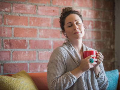 Young Woman Listening to a Relaxing Podcast Young caucasian woman listening to a meditative podcast, taking a deep inhale, while sitting on her couch in her loft apartment and holding onto her morning coffee